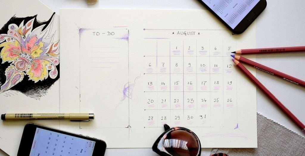 decorative image of an august calendar with mobile phones and pens scattered on top